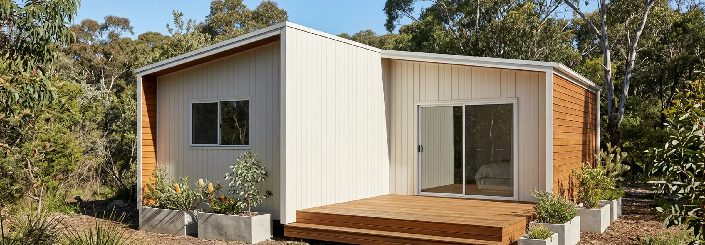 Render of the 3 bedroom, 1 bathroom Plan H in cream cladding with timber end walls and a timber deck, among native garden beds and bushland.